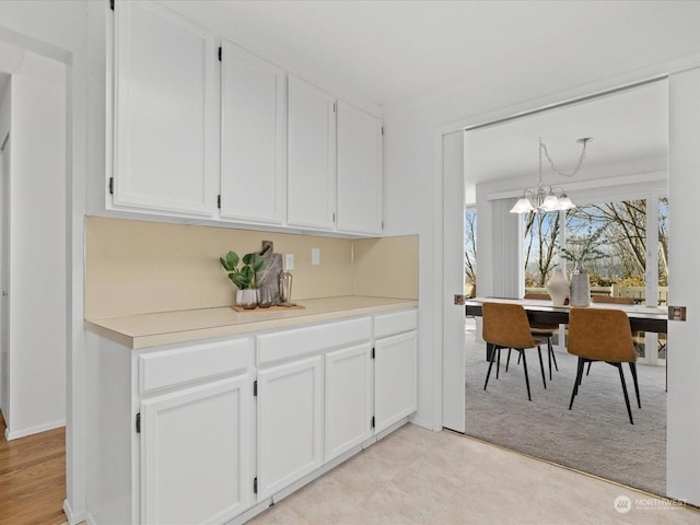 kitchen featuring white cabinets, pendant lighting, light carpet, and a chandelier