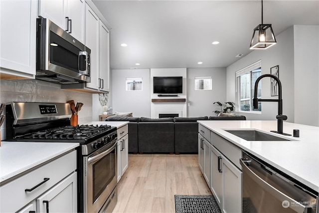 kitchen with pendant lighting, sink, light hardwood / wood-style flooring, backsplash, and stainless steel appliances