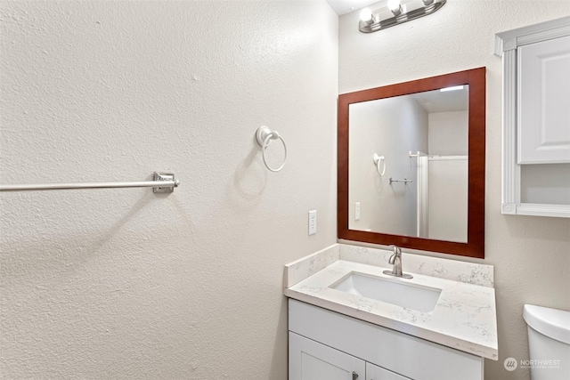 bathroom featuring a shower with door, vanity, and toilet