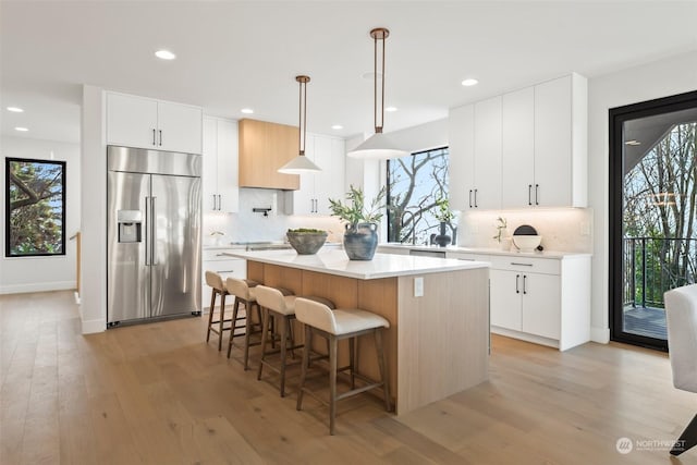 kitchen with pendant lighting, built in refrigerator, light wood-type flooring, a kitchen island, and white cabinetry