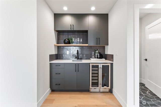 bar with sink, beverage cooler, tasteful backsplash, gray cabinets, and light wood-type flooring