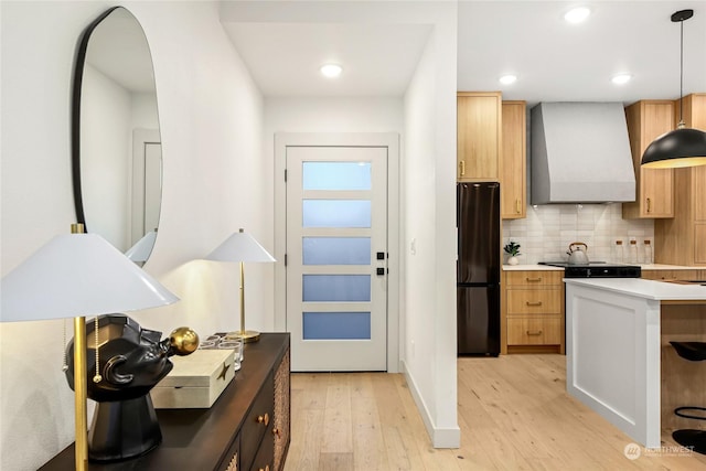 kitchen featuring black refrigerator, tasteful backsplash, wall chimney exhaust hood, pendant lighting, and light hardwood / wood-style floors