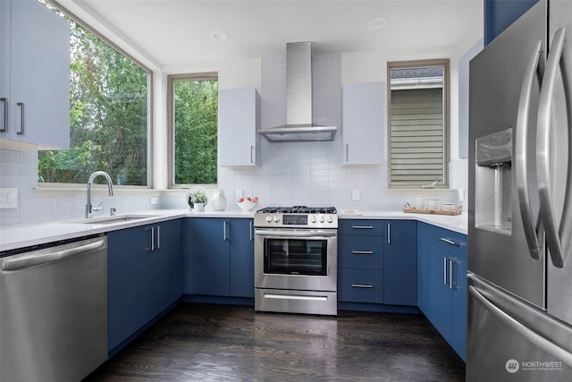 kitchen with sink, stainless steel appliances, wall chimney range hood, dark hardwood / wood-style floors, and blue cabinets