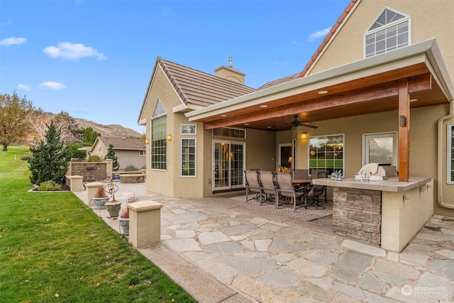 rear view of house with an outdoor kitchen, ceiling fan, a mountain view, a patio, and a lawn