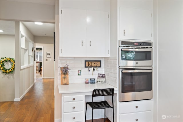 kitchen featuring white cabinets, wood-type flooring, double oven, and tasteful backsplash