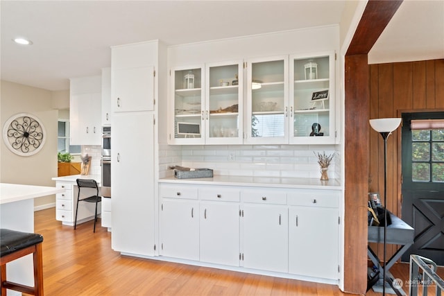 bar featuring white cabinets, decorative backsplash, double oven, and light hardwood / wood-style flooring