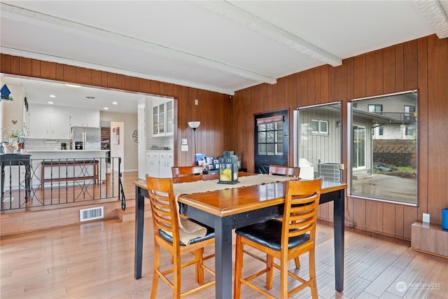 dining area with beamed ceiling, light hardwood / wood-style flooring, and wooden walls