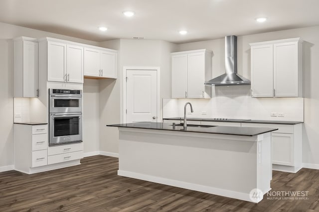 kitchen with double oven, wall chimney exhaust hood, sink, and white cabinets