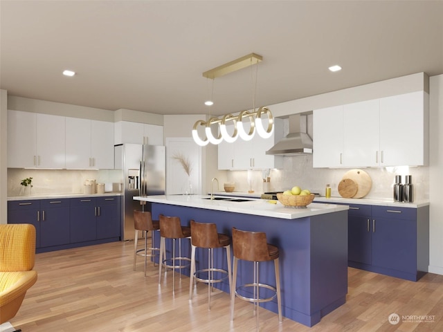 kitchen featuring a center island with sink, wall chimney exhaust hood, white cabinets, and decorative light fixtures