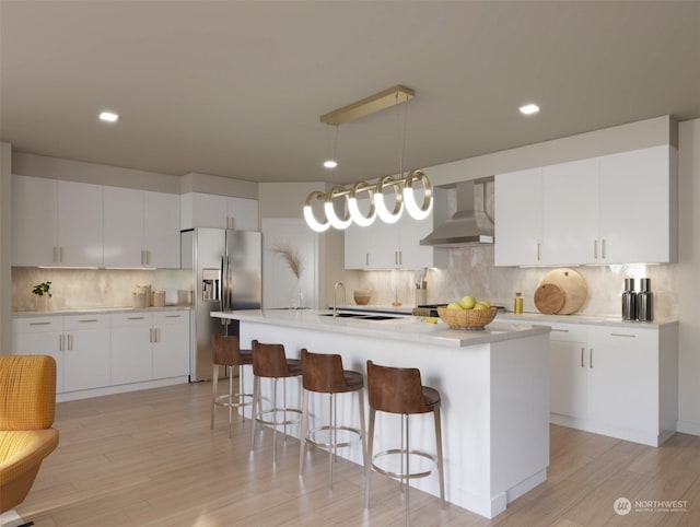 kitchen with a center island with sink, white cabinets, hanging light fixtures, and wall chimney range hood