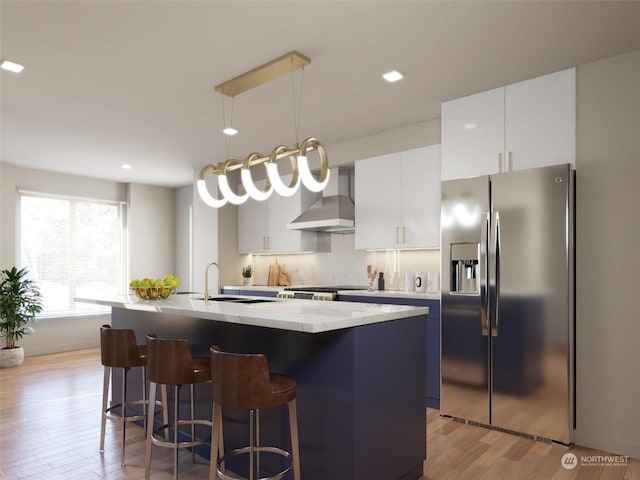 kitchen featuring white cabinets, wall chimney exhaust hood, an island with sink, and stainless steel refrigerator with ice dispenser