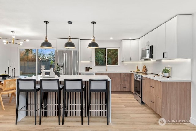 kitchen featuring white cabinets, stainless steel appliances, plenty of natural light, and hanging light fixtures