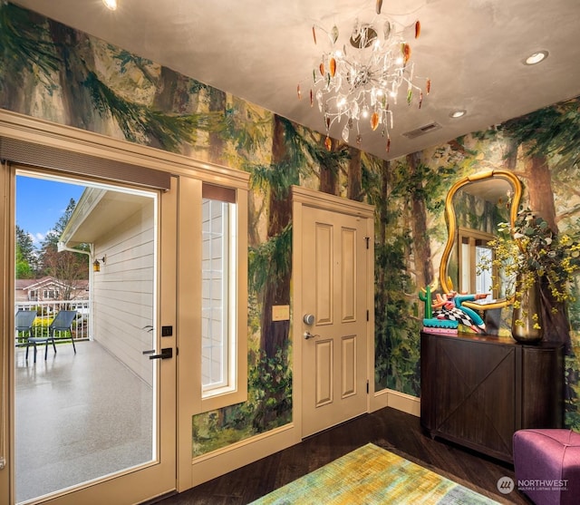 entryway with a notable chandelier, wood finished floors, visible vents, baseboards, and wallpapered walls