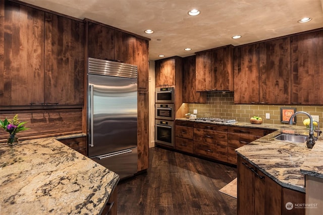 kitchen with dark wood-style flooring, stainless steel appliances, decorative backsplash, a sink, and light stone countertops