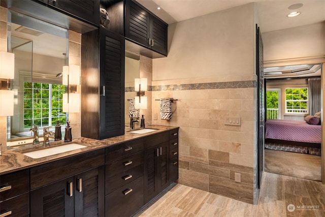 bathroom featuring ensuite bathroom, double vanity, a sink, and tile walls