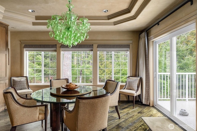 dining space with ornamental molding, a raised ceiling, hardwood / wood-style flooring, and a notable chandelier