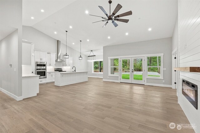 unfurnished living room featuring high vaulted ceiling, sink, ceiling fan, light hardwood / wood-style floors, and a large fireplace