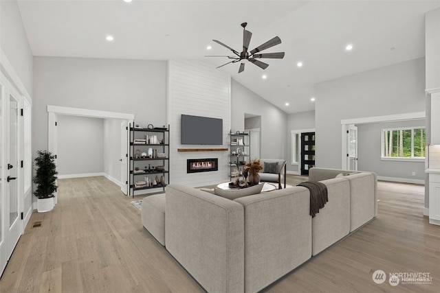 living room featuring light wood-type flooring, a large fireplace, high vaulted ceiling, and ceiling fan