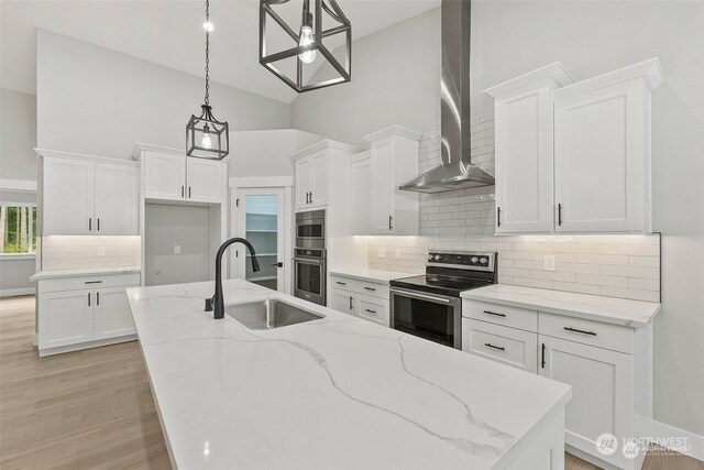 kitchen featuring sink, wall chimney range hood, decorative light fixtures, white cabinets, and appliances with stainless steel finishes