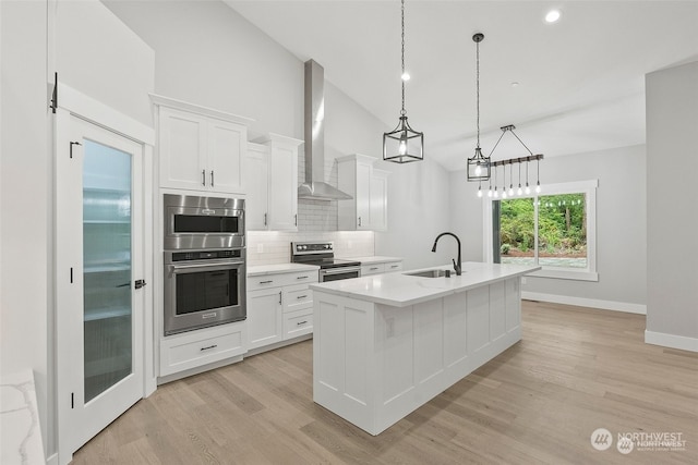 kitchen featuring stainless steel appliances, white cabinetry, wall chimney exhaust hood, and a center island with sink