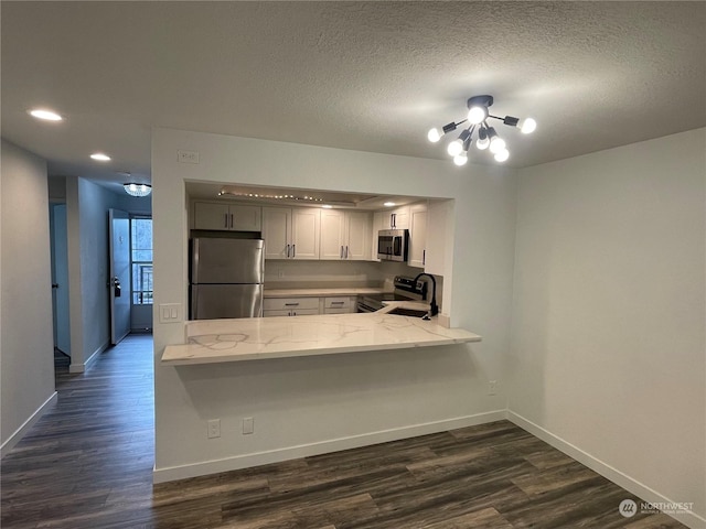 kitchen with white cabinetry, light stone countertops, dark hardwood / wood-style floors, kitchen peninsula, and appliances with stainless steel finishes