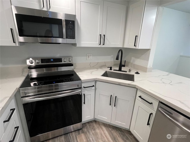 kitchen with light stone countertops, stainless steel appliances, sink, white cabinets, and hardwood / wood-style floors