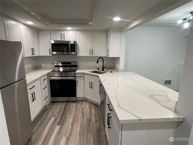 kitchen featuring sink, light stone counters, kitchen peninsula, white cabinets, and appliances with stainless steel finishes