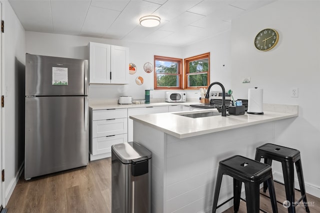 kitchen featuring hardwood / wood-style flooring, stainless steel refrigerator, white cabinets, and a breakfast bar