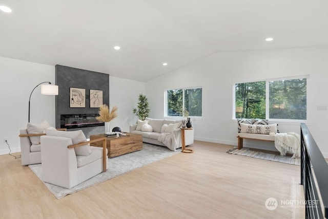 living room featuring a fireplace, light wood-type flooring, vaulted ceiling, and a wealth of natural light