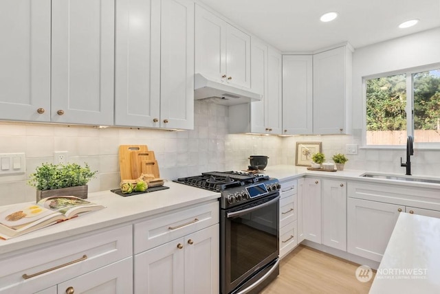 kitchen featuring white cabinetry, sink, stainless steel gas range oven, decorative backsplash, and light wood-type flooring