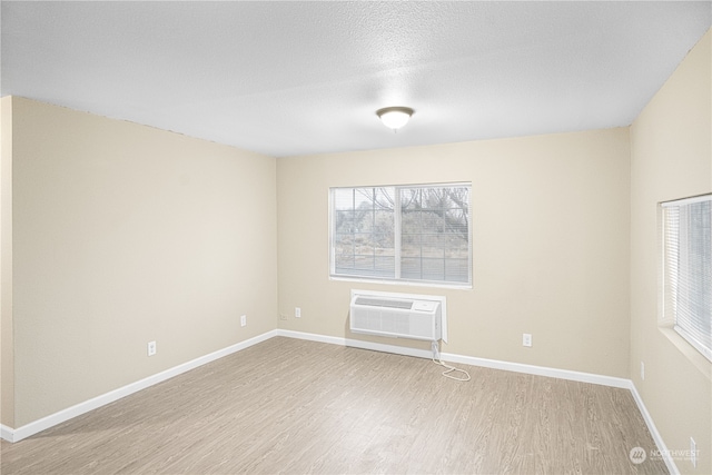 spare room featuring an AC wall unit, a textured ceiling, and light wood-type flooring