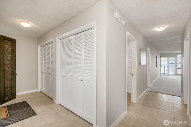 hall featuring light tile patterned floors, a textured ceiling, and baseboards