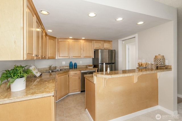 kitchen featuring light brown cabinetry, a kitchen breakfast bar, appliances with stainless steel finishes, a peninsula, and a sink