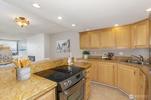 kitchen with a sink, stainless steel range with electric cooktop, light tile patterned flooring, light countertops, and a brick fireplace