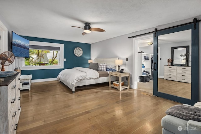 bedroom featuring wood-type flooring, a barn door, a textured ceiling, and ceiling fan