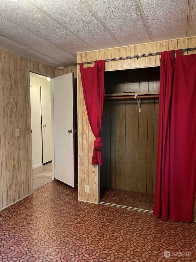 unfurnished bedroom featuring a textured ceiling, wooden walls, and a closet