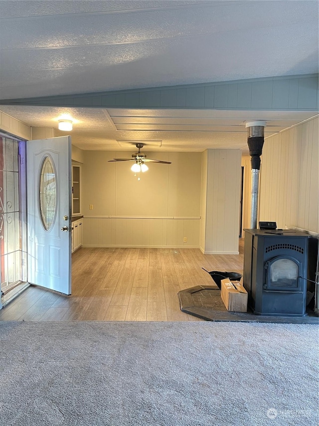 unfurnished living room featuring ceiling fan, light hardwood / wood-style floors, a wood stove, and a textured ceiling