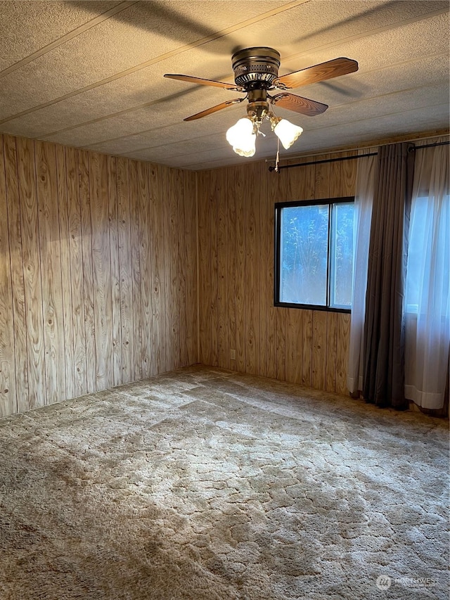 carpeted empty room with a textured ceiling, ceiling fan, and wood walls