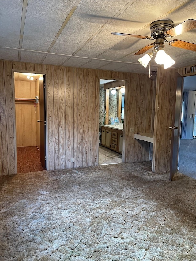 unfurnished living room featuring light colored carpet, ceiling fan, and wooden walls