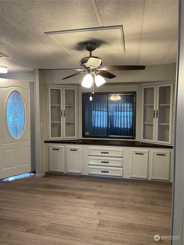 bar with white cabinets, a textured ceiling, and light wood-type flooring