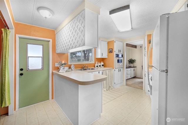 kitchen with kitchen peninsula, a textured ceiling, white appliances, sink, and white cabinets