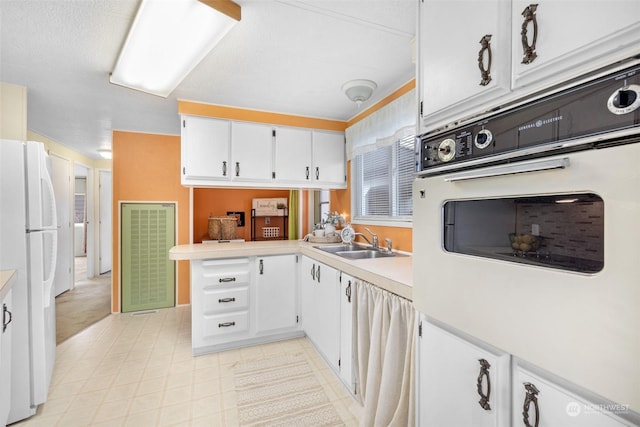 kitchen with kitchen peninsula, white cabinetry, white appliances, and sink