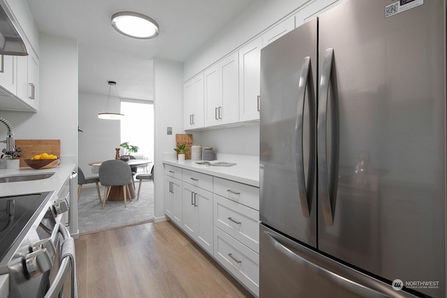 kitchen with appliances with stainless steel finishes, sink, decorative light fixtures, light hardwood / wood-style flooring, and white cabinetry