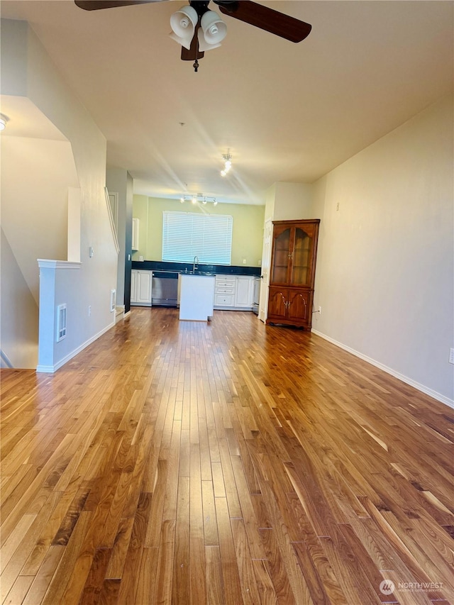 unfurnished living room with wood-type flooring, ceiling fan, and sink