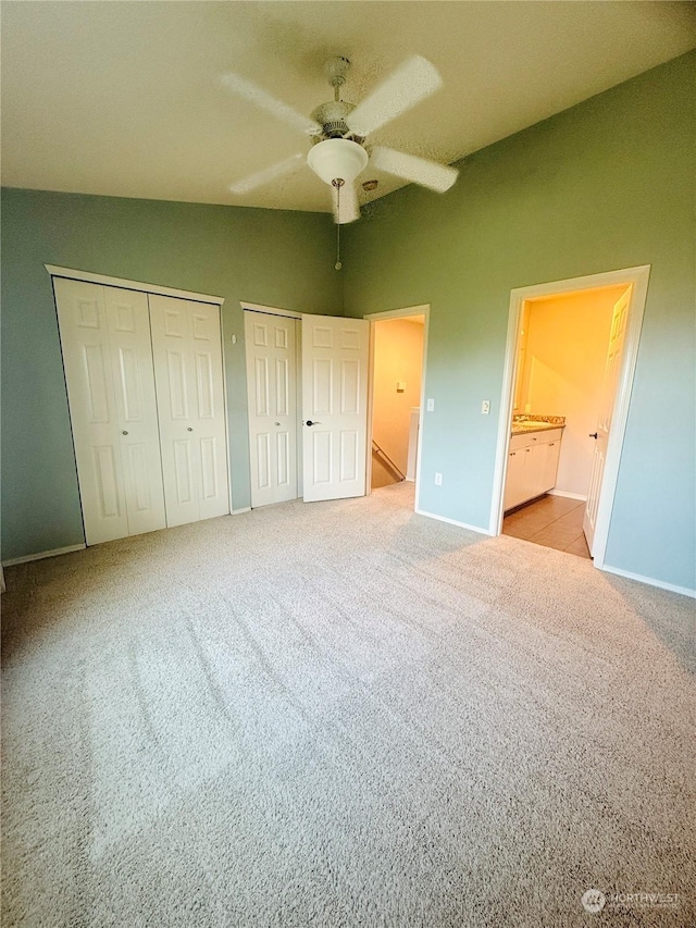 unfurnished bedroom featuring connected bathroom, ceiling fan, light carpet, and multiple closets