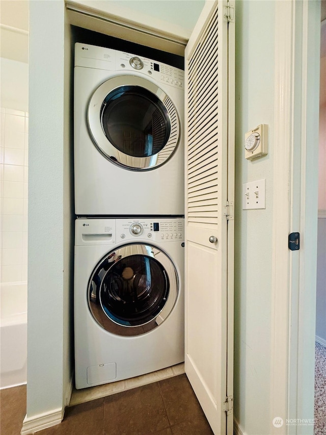 laundry area featuring dark tile patterned floors and stacked washer and dryer