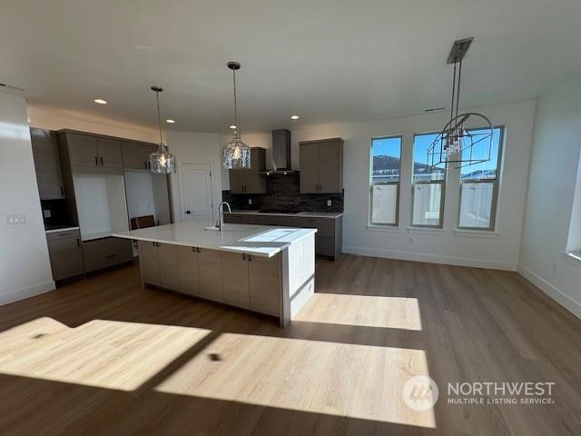 kitchen featuring hanging light fixtures, a kitchen island with sink, wall chimney range hood, and decorative backsplash