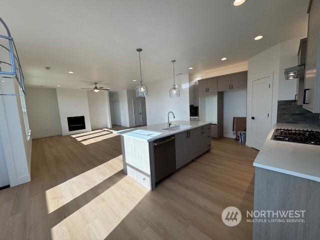 kitchen with light wood-type flooring, an island with sink, dishwasher, and sink