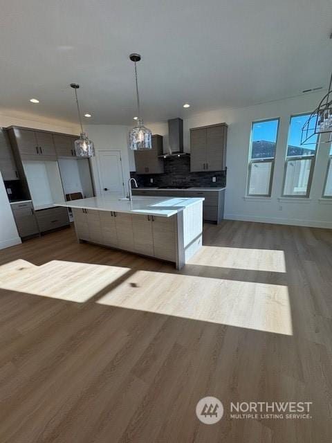 kitchen featuring decorative light fixtures, backsplash, an island with sink, gray cabinetry, and wall chimney exhaust hood