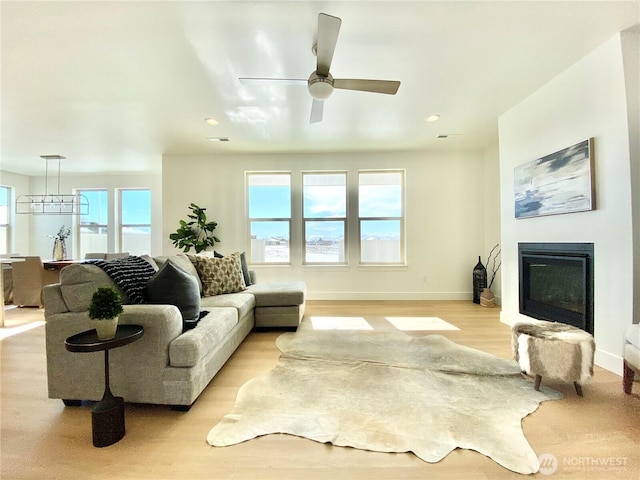 living room with baseboards, a ceiling fan, a glass covered fireplace, light wood-type flooring, and recessed lighting